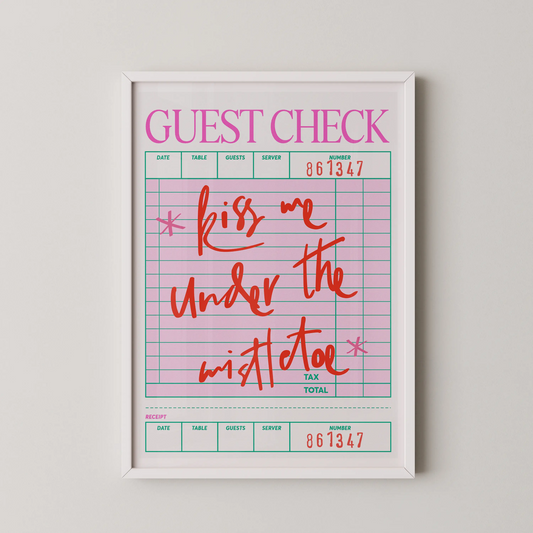 A Pop Art style guest check quote wall art featuring the text 'kiss me under the mistletoe' in coral red hand-lettering on a pink grid.