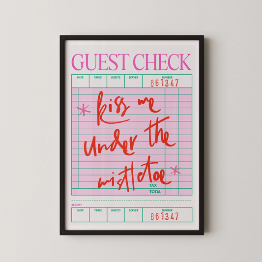 A Pop Art style guest check quote wall art featuring the text 'kiss me under the mistletoe' in coral red hand-lettering on a pink grid.
