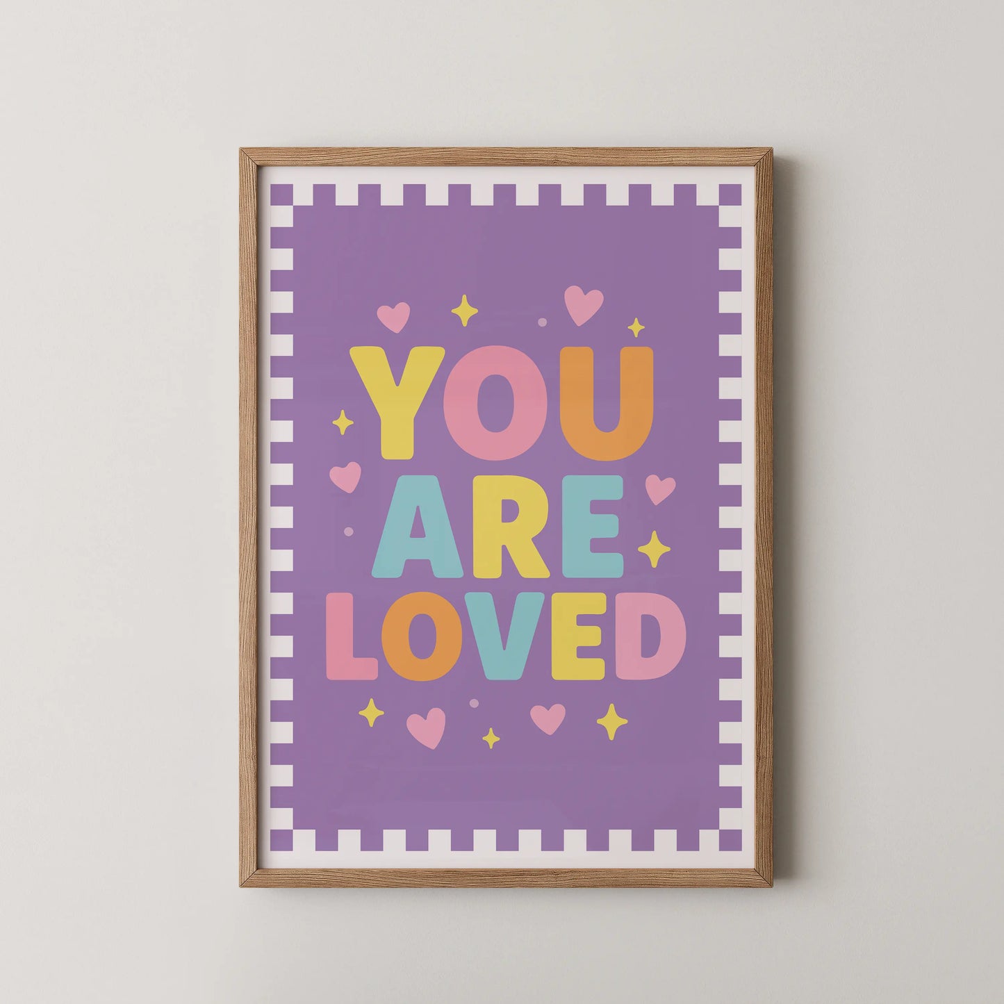 A modern typographic poster featuring the phrase "YOU ARE LOVED" in bold, rounded letters, surrounded by tiny hearts and sparkles on a soft pastel background.